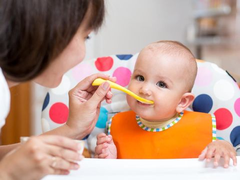 smiling baby girl eating food with mom on kitchen