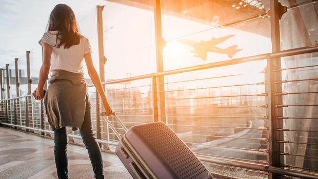 Young woman pulling suitcase in  airport terminal. Copy space