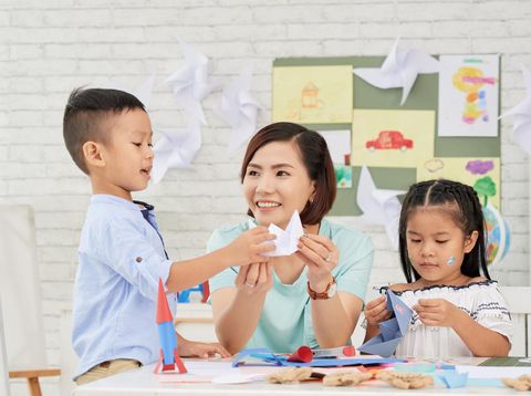 Young Asian woman teaching children how to make paper ships at art craft