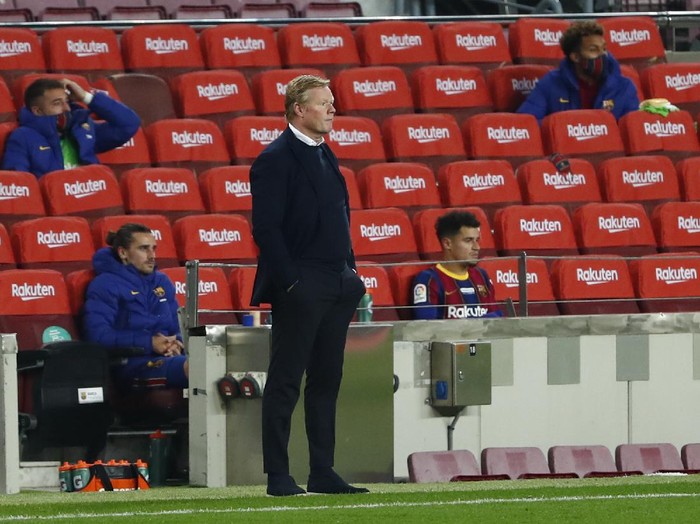 Barcelonas head coach Ronald Koeman watches his players from the side lines with Barcelonas Antoine Griezmann, left and Barcelonas Philippe Coutinho, right, behind in the substitutes area during the Spanish La Liga soccer match between Barcelona and Valencia at the Camp Nou stadium in Barcelona, Spain, Saturday, Dec. 19, 2020. (AP Photo/Joan Monfort)