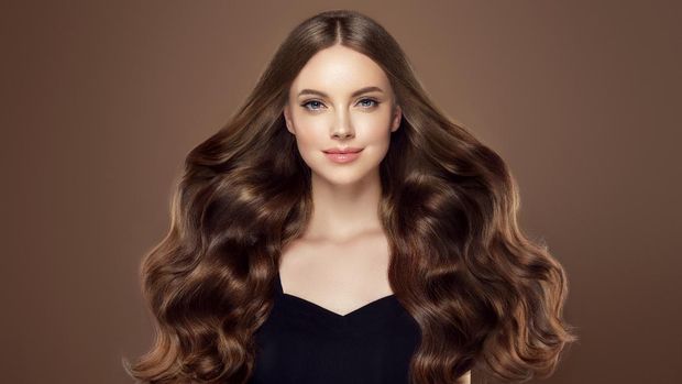 Young, brown haired woman  with voluminous hair.Beautiful model with long, dense, curly hairstyle and vivid makeup. Perfect dense, wavy,and shiny hair. Hairdressing art, hair care and beauty products.