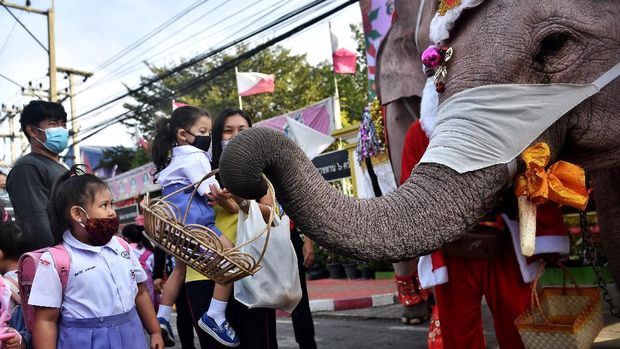 A student (L) looks up at an elephant (R) from the Ayutthaya Elephant Palace, dressed in a Santa Claus costume and wearing a face mask, as it holds out a basket containing face masks outside the Jirasat Wittaya School in the central Thai province of Ayutthaya on December 23, 2020. (Photo by Lillian SUWANRUMPHA / AFP)