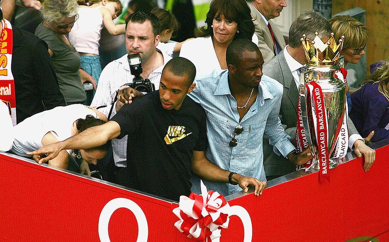 LONDON - MAY 16:  Thierry Henry (L) and Patrick Vieira are seen at the front of the bus outside the Islington Town Hall during the Arsenal Football Club victory parade to show the League Champions with their FA Barclaycard Premiership Trophy on May 16, 2004 in Highbury, London. (Photo by Clive Mason/Getty Images)