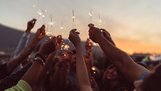 Group of friends holding burning sparklers against the sky