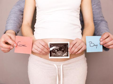 Pregnant woman with her husband holding ultrasound scan and blue and red post its with words boy or girl
