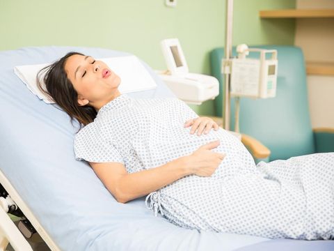 Portrait of a beautiful young pregnant woman trying to breath to soothe the pain of her labor contractions in a hospital