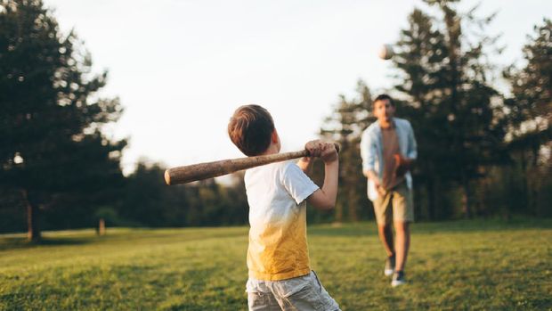 Young father sharing basics of baseball with his little boy, outdoors in the park
