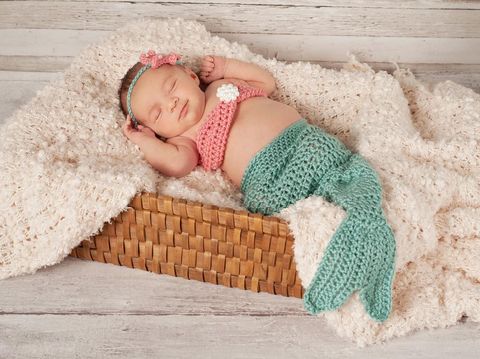 Adorable two months baby girl relaxing in bedroom on knitted blanket on a sunny morning