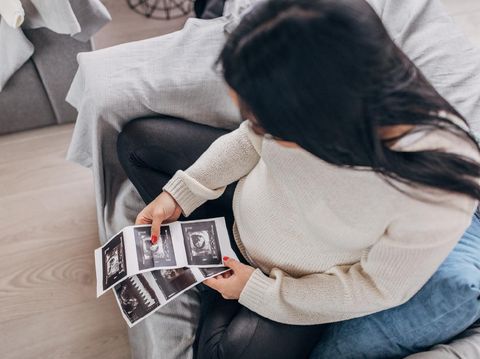 One woman, beautiful pregnant woman sitting at home, holding ultrasound pictures.