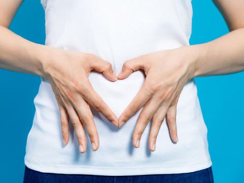 young woman who makes a heart shape by hands on her stomach.