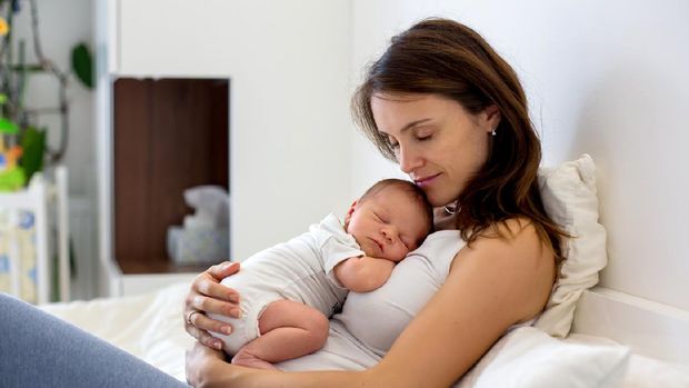 Tired mother holding her newborn child at home after tying to pump.