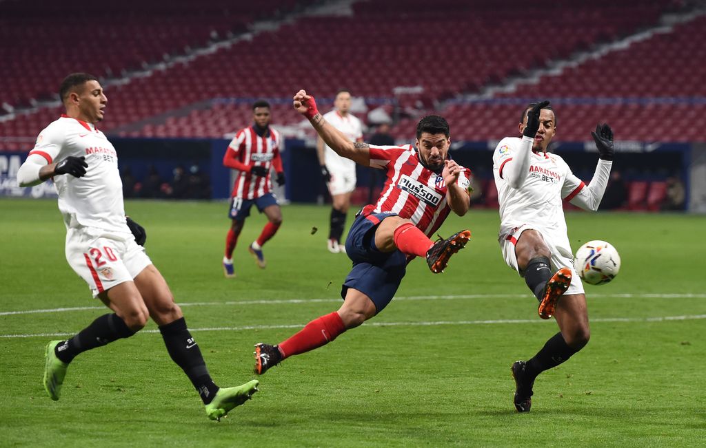 MADRID, SPAIN - JANUARY 12: Luis Suarez of Atletico de Madrid shoots as Jules Kounde of Sevilla FC attempts to block during the La Liga Santander match between Atletico de Madrid and Sevilla FC at Estadio Wanda Metropolitano on January 12, 2021 in Madrid, Spain. Sporting stadiums around Spain remain under strict restrictions due to the Coronavirus Pandemic as Government social distancing laws prohibit fans inside venues resulting in games being played behind closed doors. (Photo by Denis Doyle/Getty Images)