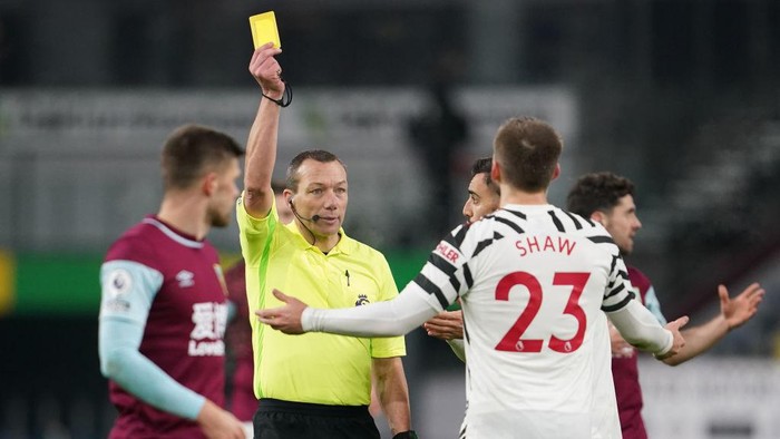 BURNLEY, ENGLAND - JANUARY 12: Referee, Kevin Friend shows Luke Shaw of Manchester United a yellow card during the Premier League match between Burnley and Manchester United at Turf Moor on January 12, 2021 in Burnley, England. Sporting stadiums around England remain under strict restrictions due to the Coronavirus Pandemic as Government social distancing laws prohibit fans inside venues resulting in games being played behind closed doors. (Photo by Jon Super - Pool/Getty Images)