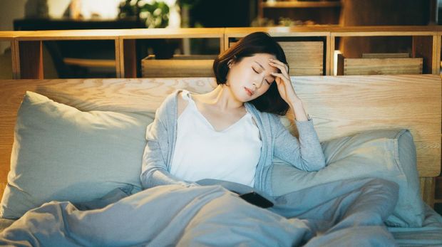 Young Asian woman feeling sick and suffering from a headache, lying on the bed and taking a rest at home