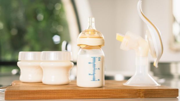 Baby bottle with milk and manual breast pump.  A lot of full bottles with breast milk on the background.  Mother's milk - the most healthy food for newborn
