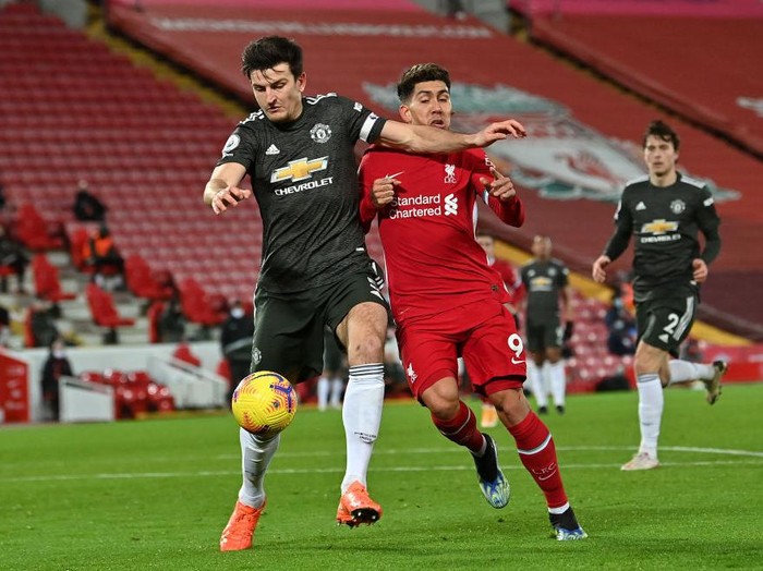 LIVERPOOL, ENGLAND - JANUARY 17: Harry Maguire of Manchester United is tackled by Roberto Firmino of Liverpool during the Premier League match between Liverpool and Manchester United at Anfield on January 17, 2021 in Liverpool, England. Sporting stadiums around England remain under strict restrictions due to the Coronavirus Pandemic as Government social distancing laws prohibit fans inside venues resulting in games being played behind closed doors. (Photo by Paul Ellis - Pool/Getty Images)