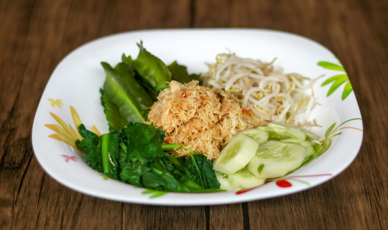 Sayur urap on wood background. Cooked vegetables with spiced grated coconut. Indonesian traditional food.