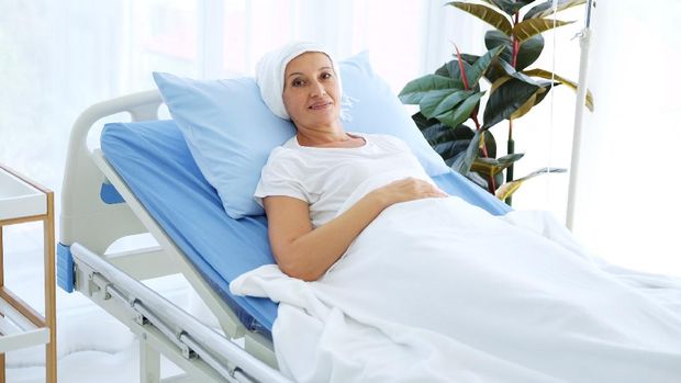 Smiling Caucasian Elderly Mother in white headscarf is laying on bed in hospital after chemotherapy because she is suffering from cancer or Leukemia patient.