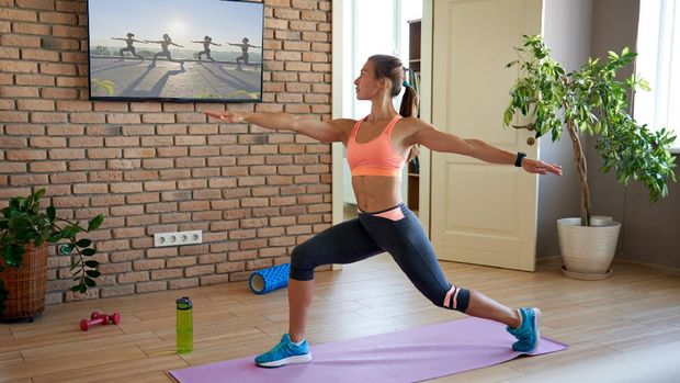 Fit sporty active young woman learning warrior yoga pose watching live streaming online workout exercise training weightloss class sport tv at home in living room. Fitness tutorialÂ  livestream concept
