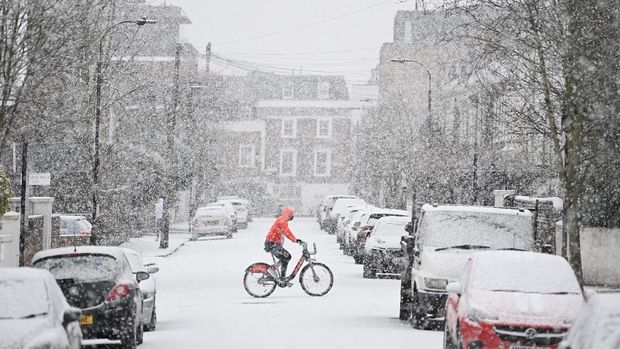 A cyclist crosses a snow covered road in west London on January 24, 2021, as the capital experiences a rare covering of snow on Sunday. (Photo by DANIEL LEAL-OLIVAS / AFP)