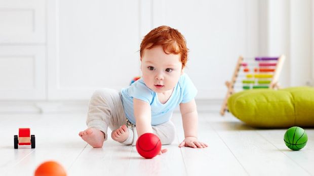 cute infant baby crawling on the floor at home, playing with colorful balls