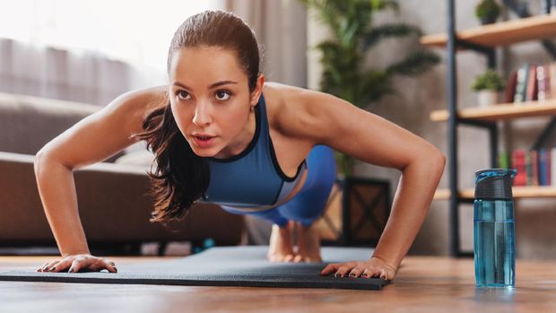 Beautiful young sports lady doing push ups while workout at home