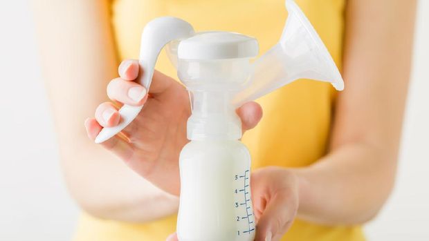 Young mother hands holding full plastic breast pump bottle. Closeup. Preparing milk for baby feeding. Front view.