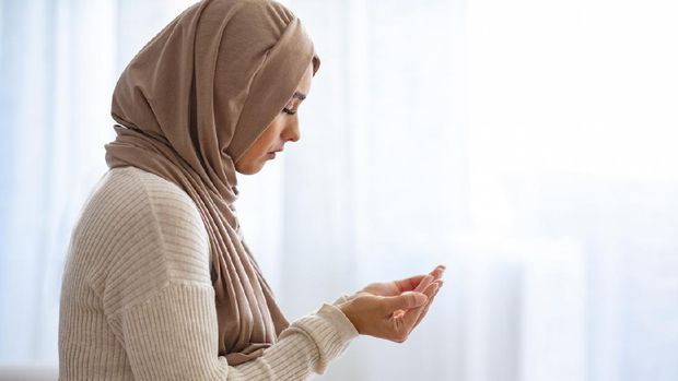 Young Woman Praying. Young Muslim woman praying, indoors. Young Muslim woman in beige hijab and traditional clothes praying for Allah, copy space. Arab Muslim woman praying