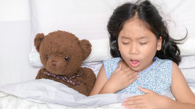 Little girl is coughing and sore throat lying on bed with toy bear, Health care concept