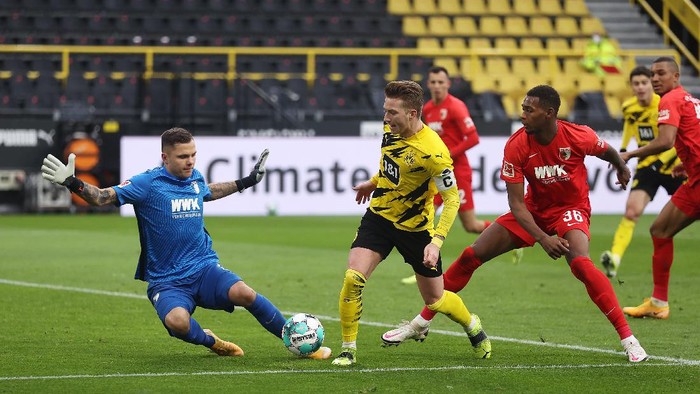 DORTMUND, GERMANY - JANUARY 30: Marco Reus of Borussia Dortmund is put under pressure by Rafal Gikiewicz (L) and Reece Oxford (R) of Augsburg during the Bundesliga match between Borussia Dortmund and FC Augsburg at Signal Iduna Park on January 30, 2021 in Dortmund, Germany. Sporting stadiums around Germany remain under strict restrictions due to the Coronavirus Pandemic as Government social distancing laws prohibit fans inside venues resulting in games being played behind closed doors. (Photo by Lars Baron/Getty Images)