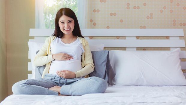 Happy pregnant mother touching beautiful belly with love, smile face on bed at home. prenatal, pregnancy, motherhood, expect concept. Young pregnancy girl and baby or fetus has good health, copy space