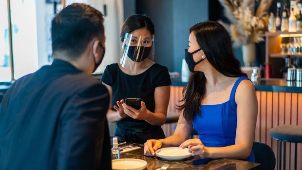 Asian waitress with face mask and face shield taking food orders from customers.
