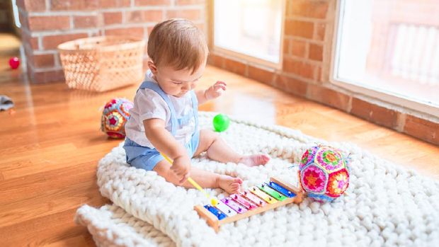 Beautiful toddler sitting on the blanket playing xylophone smiling at kindergarten