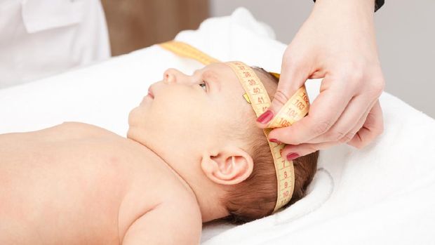 Close-up shot of pediatrician examines two months baby boy. Doctor using measurement tape checking baby head size