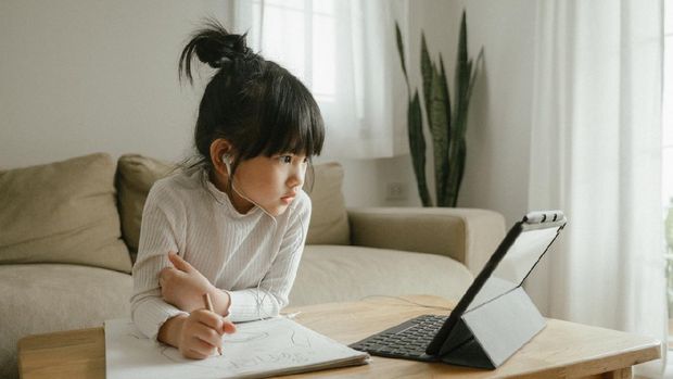Young woman wearing headphones learning using digital tablet and teleconferencing apps in living room at home