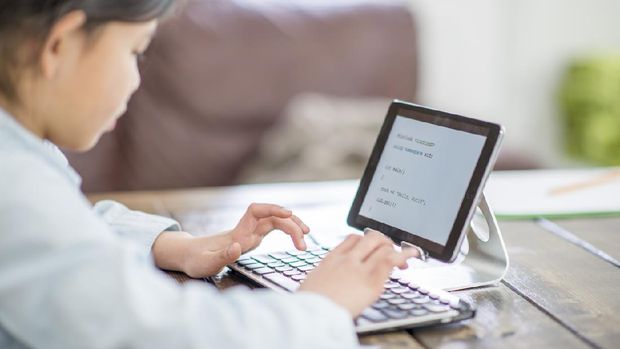 Happy young Asian family with children and their mother using computer do school homework at home.