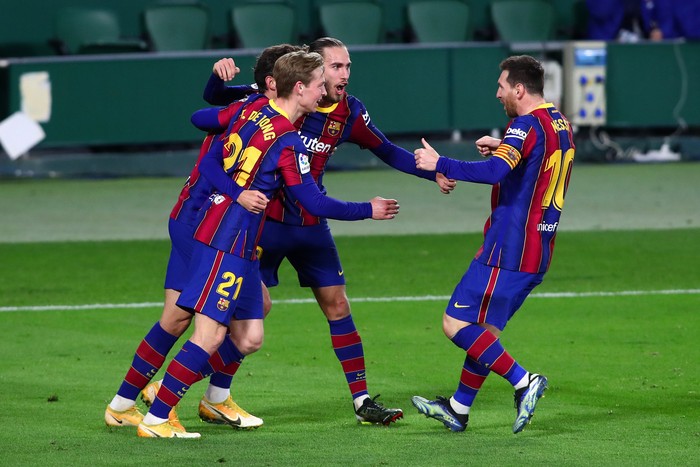SEVILLE, SPAIN - FEBRUARY 07: Trincao of FC Barcelona (L), hidden) celebrates with teammates Frenkie de Jong, Oscar Mingueza and Lionel Messi of FC Barcelona after scoring their teams third goal during the La Liga Santander match between Real Betis and FC Barcelona at Estadio Benito Villamarin on February 07, 2021 in Seville, Spain. Sporting stadiums around Spain remain under strict restrictions due to the Coronavirus Pandemic as Government social distancing laws prohibit fans inside venues resulting in games being played behind closed doors. (Photo by Fran Santiago/Getty Images)