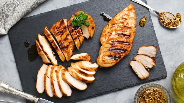 Grilled chicken fillets on slate plate. Gray concrete background