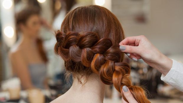 Beautiful, with long, red-haired hairy girl, hairdresser weaves a French braid, close-up in a beauty salon. Professional hair care and creating hairstyles.