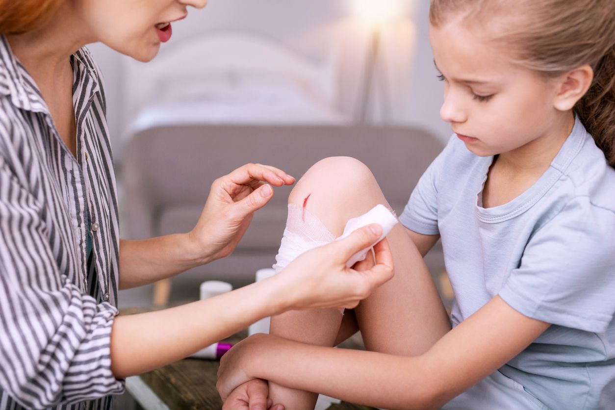 Loving mother. Nice pleasant woman looking at her daughters bruise while applying ointment on it