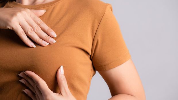 Woman hand checking lumps on her breast for signs of breast cancer on gray background. Healthcare concept.