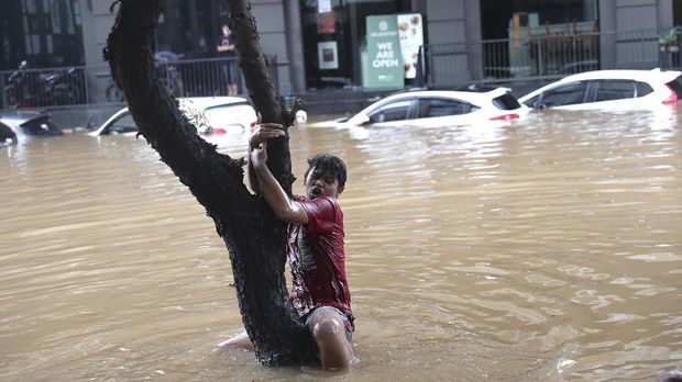 A man grabs a tree to keep from being swept away by flood water through a flooded neighborhood following heavy rains in Jakarta, Indonesia, Saturday, Feb. 20, 2021. Heavy downpours combined with poor city sewage planning often causes heavy flooding in parts of greater Jakarta. (AP Photo/Tatan Syuflana)