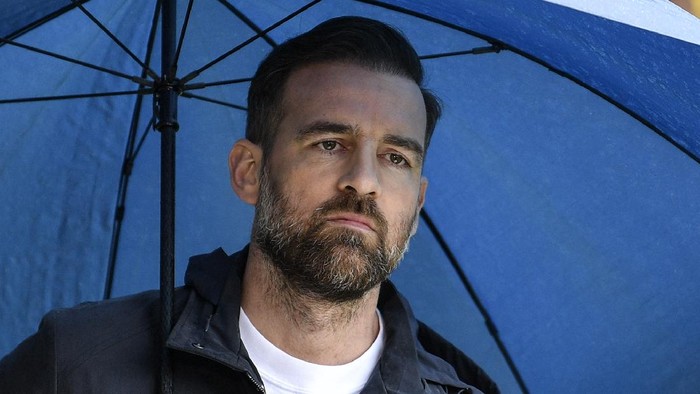 FILE - In this Saturday, April 27, 2019 file photo, Christoph Metzelder watches under an umbrella prior the German Bundesliga soccer match between Borussia Dortmund and FC Schalke 04 in Dortmund, Germany. Former Germany defender Christoph Metzelder will stand trial on charges of possession and distribution of child pornography on April 29, 2021. He faces 29 charges of attempted distribution of child pornography to another person, and one charge of the possession of child and youth pornography.  (AP Photo/Martin Meissner, file)