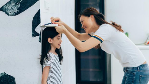 Little 5 years old girl measure a height of boy by scale on the wall