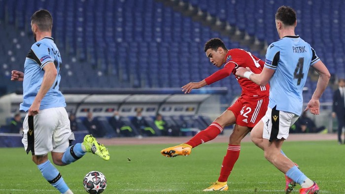 ROME, ITALY - FEBRUARY 23: Jamal Musiala of FC Bayern Muenchen scores their sides second goal under pressure from Patric of S.S. Lazio during the UEFA Champions League Round of 16 match between Lazio Roma and Bayern München at Olimpico Stadium on February 23, 2021 in Rome, Italy. Sporting stadiums around Italy remain under strict restrictions due to the Coronavirus Pandemic as Government social distancing laws prohibit fans inside venues resulting in games being played behind closed doors. (Photo by Alexander Hassenstein/Getty Images)