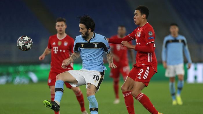 Liga Champions ROME, ITALY - FEBRUARY 23: Luis Alberto of S.S. Lazio battles for possession with Jamal Musiala of FC Bayern Muenchen during the UEFA Champions League Round of 16 match between Lazio Roma and Bayern München at Olimpico Stadium on February 23, 2021 in Rome, Italy. Sporting stadiums around Italy remain under strict restrictions due to the Coronavirus Pandemic as Government social distancing laws prohibit fans inside venues resulting in games being played behind closed doors. (Photo by Paolo Bruno/Getty Images)