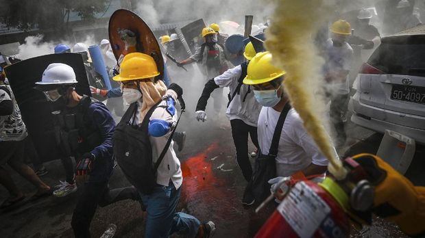 A protester uses a fire extinguisher as others holding homemade shields run during a demonstration against the military coup in Yangon on March 3, 2021. (Photo by STR / AFP)