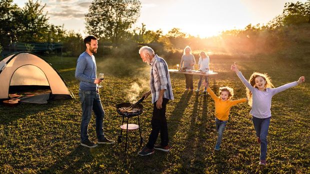 Happy multi-generation family enjoying while making barbecue during garden party at sunset. Kids are having fun.