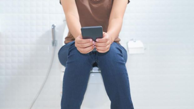 Woman sitting on toilet and using smartphone - constipation concept.