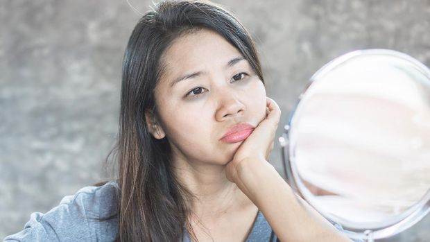unhappy Asian woman age 40 checking her dark eyes circle problem in mirror
